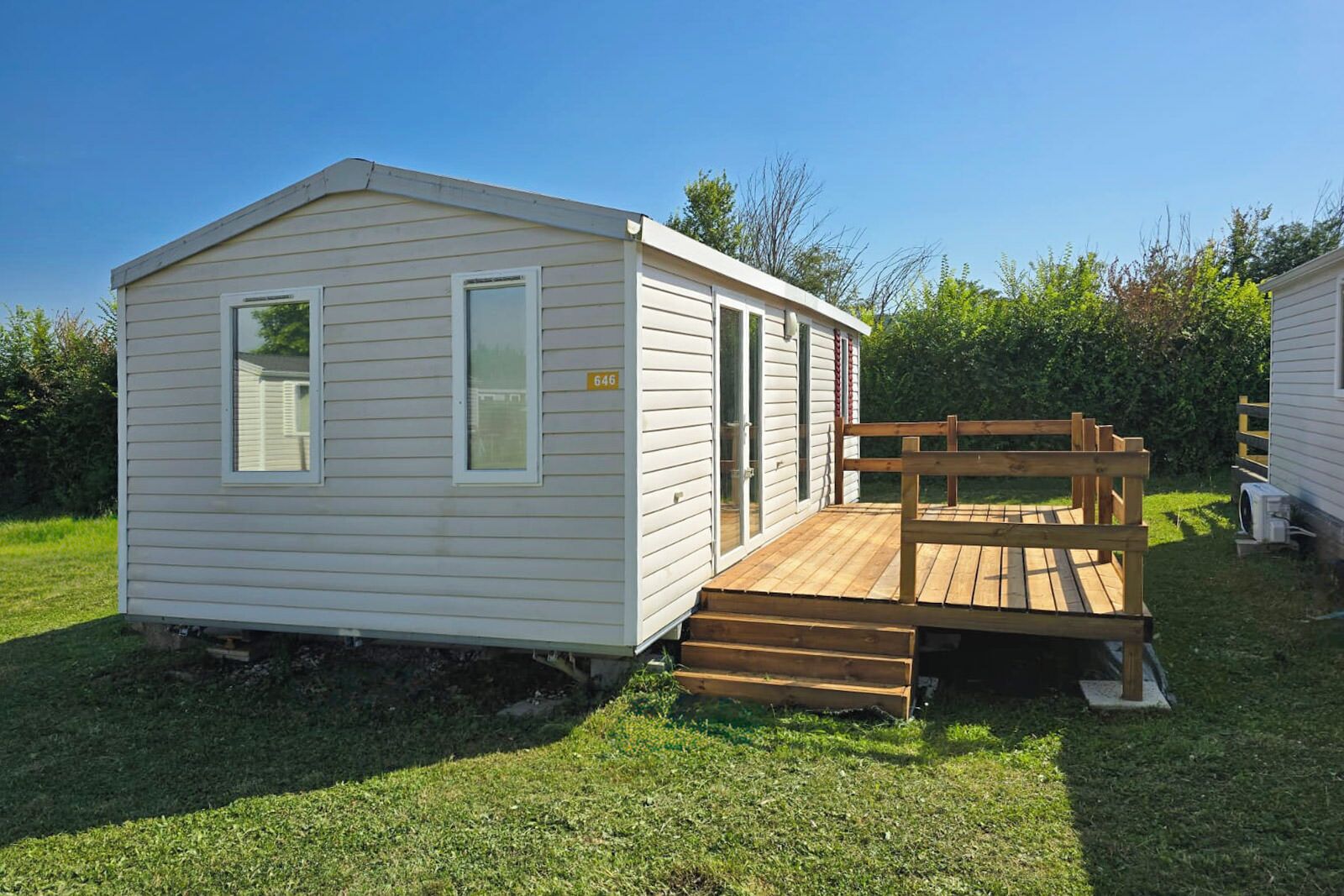 Une petite maison mobile d’un seul étage, dotée d’une terrasse en bois et d’une rampe menant à l’entrée.