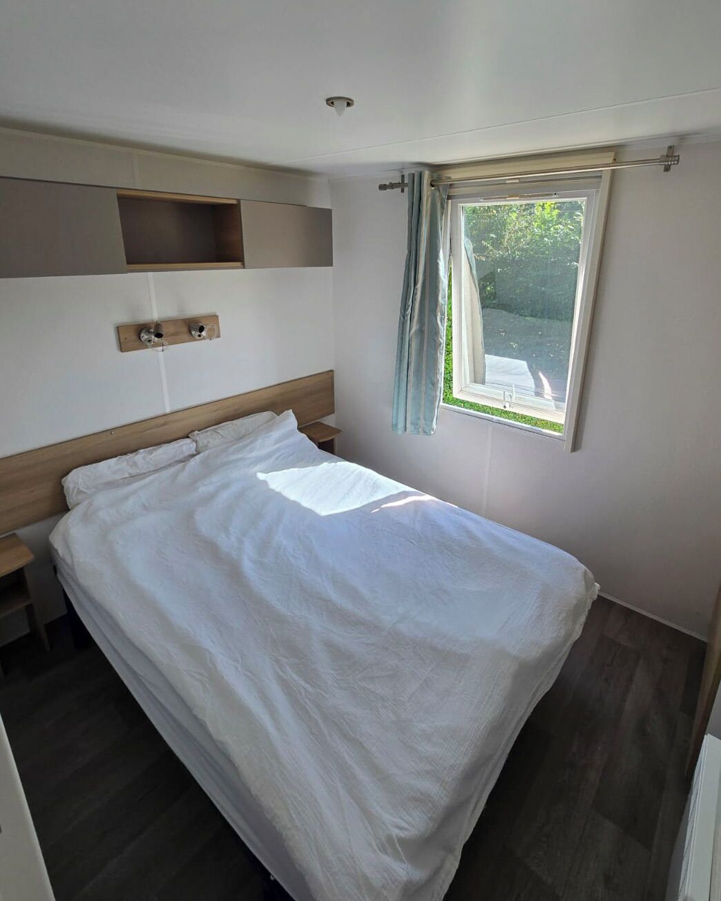 Una cama individual con cabecera de madera, una mesita de noche y una ventana con cortinas.