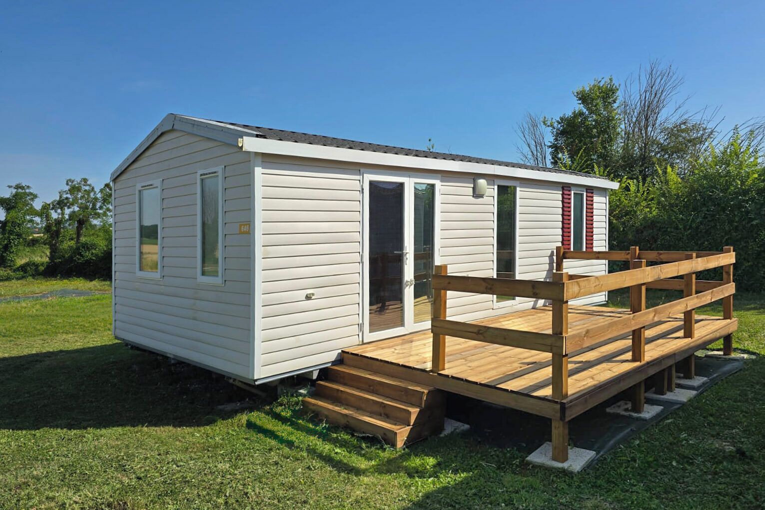 A single-story mobile home with a wooden deck and a ramp leading to the entrance.