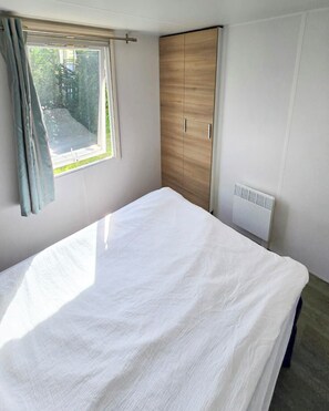 A bedroom with a bed, a wardrobe, a radiator, and a window with curtains. - Violettes - two-bedroom Parc Home combines comfort, practicality, and charm. (Lévignac-de-Guyenne)