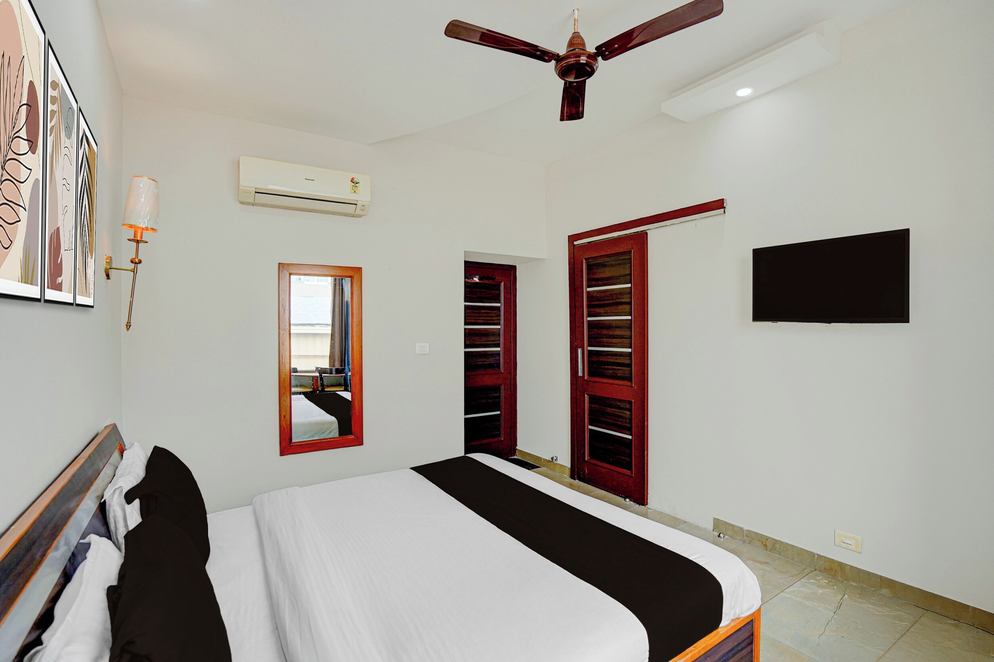 Un dormitorio con cama, ventilador de techo, unidad de aire acondicionado, espejo, armario y televisor.