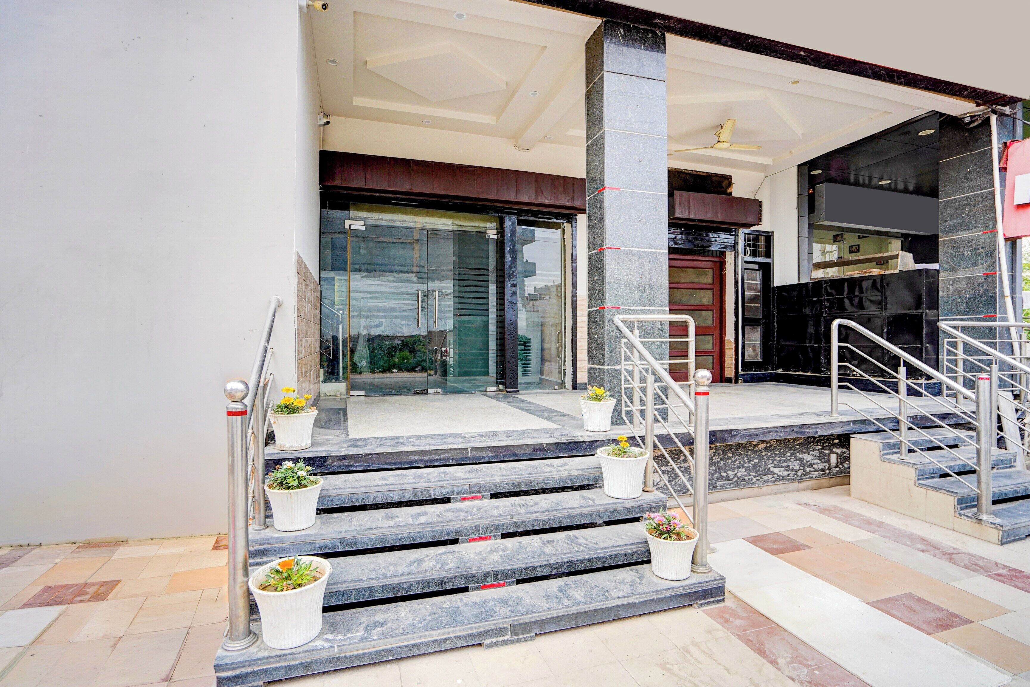 Entrada de hotel con escalones de mármol, puerta de cristal y plantas en macetas.