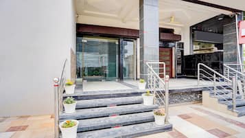 Entrada de hotel con escalones de mármol, puerta de cristal y plantas en macetas.