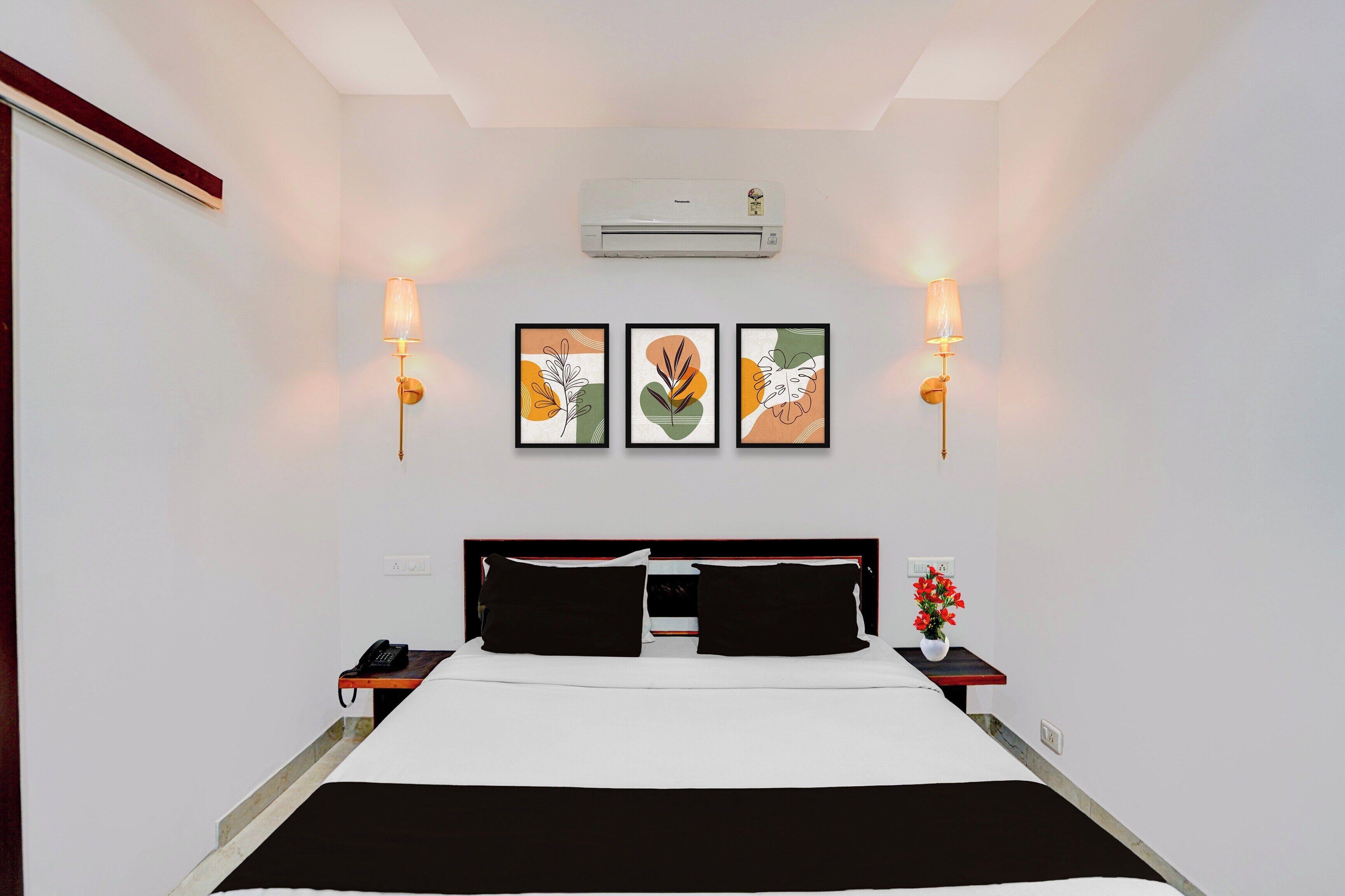 Una habitación de hotel con una cama, dos mesitas de noche, un armario auxiliar, un equipo de aire acondicionado y una obra de arte en la pared.