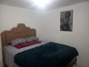 Ein Schlafzimmer mit einem Bett, einem Kopfteil, einem Kopfkissen, einer Decke und einem Poster an der Wand.
