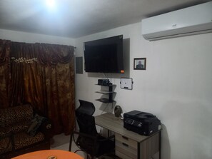 A room with a bed, a desk with a printer, a television, and a wall-mounted air conditioner. - Two Bedroom Apartments Home Flat In Jamaica Montego Bay (Montego Bay)