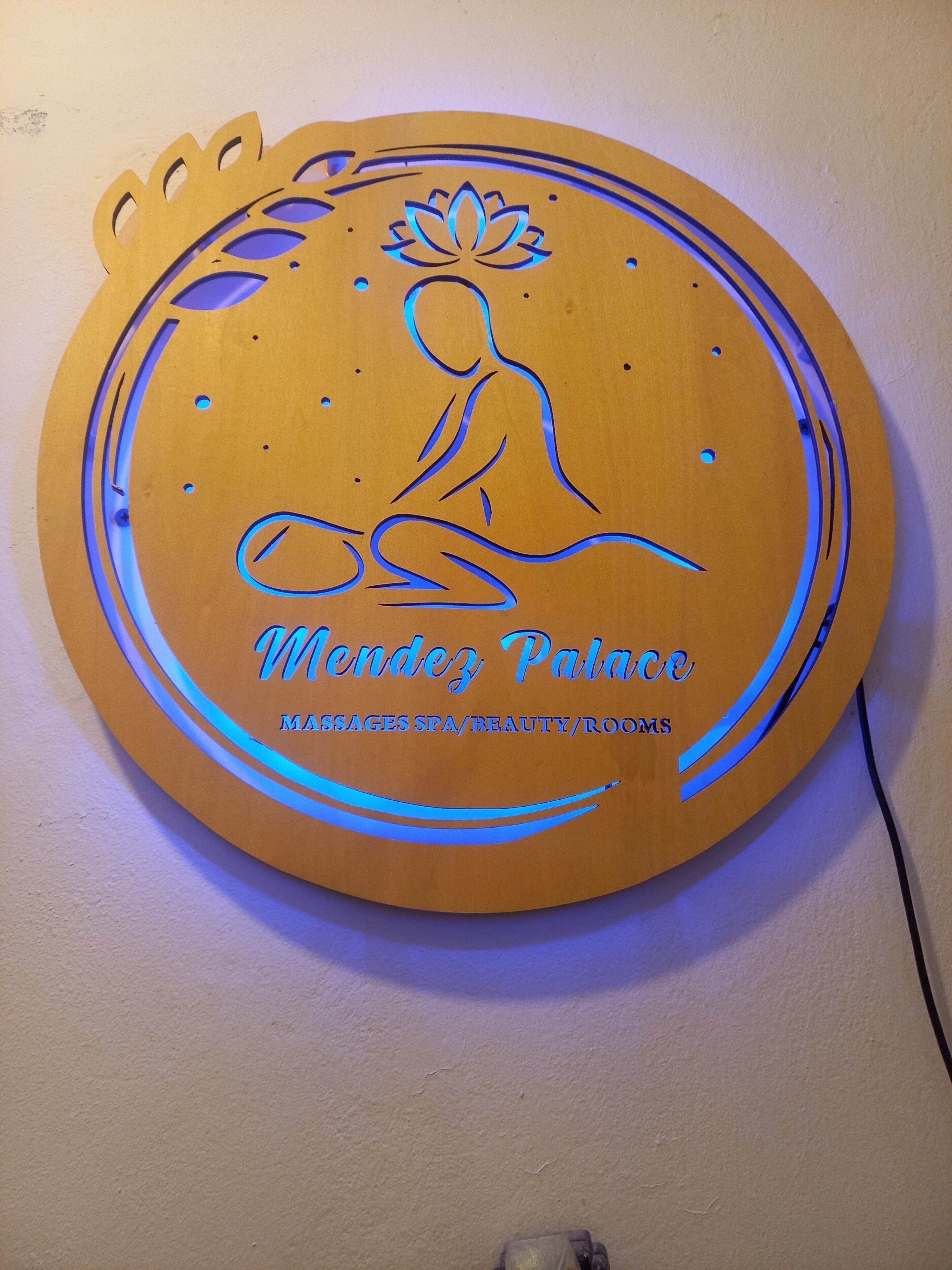Um sinal de madeira circular com uma figura meditativa e texto indicando que é para massagens, spa, serviços de beleza e quartos.