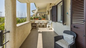 Ein überdachter Außenbereich mit Esstisch und Stühlen, einem Korbstuhl und Blick auf das Meer.