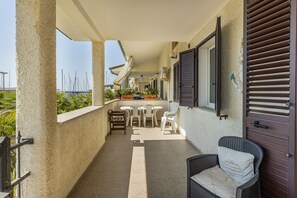 A covered outdoor area with a dining table and chairs, a wicker chair, and a view of the sea. - Holiday Home 'Sul Porto – Steps from the Sea' with Sea View, Private Terrace & AC (Grosseto)