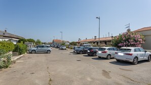 Ein Parkplatz mit mehreren Autos, Gebäude mit roten Ziegeldächern und einem wolkenlosen Himmel.
