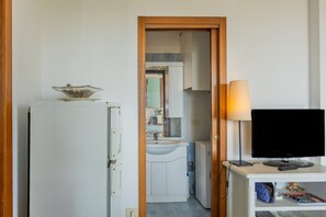 A room with a white refrigerator, a television on a stand, and a door leading to a bathroom. - Holiday Home 'Sul Porto – Steps from the Sea' with Sea View, Private Terrace & AC (Grosseto)