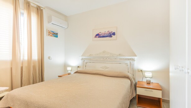 Ein Hotelzimmer mit einem Bett, zwei Nachttischen, einer Wand-Klimaanlage und einem gerahmten Bild über dem Bett.