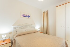 A bedroom with a bed, a nightstand, a lamp, a wardrobe, and a wall-mounted picture. - Holiday Home 'Sul Porto – Steps from the Sea' with Sea View, Private Terrace & AC (Grosseto)