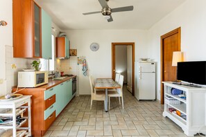 A compact kitchen with a dining area, a ceiling fan, a refrigerator, and a television on a stand. - Holiday Home 'Sul Porto – Steps from the Sea' with Sea View, Private Terrace & AC (Grosseto)