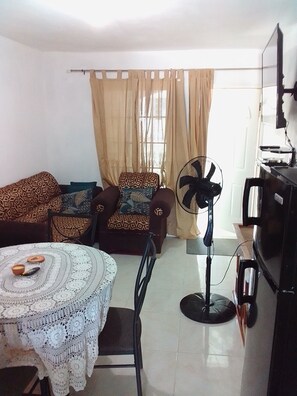 A living room with a sofa, armchair, table, fan, and TV. - THE PLAYMAKER GIRLS  NEXT GALAXY VILLA MBJ (Montego Bay)