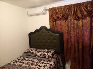 Een slaapkamer met een bed, een wandairconditioner en een gordijn.