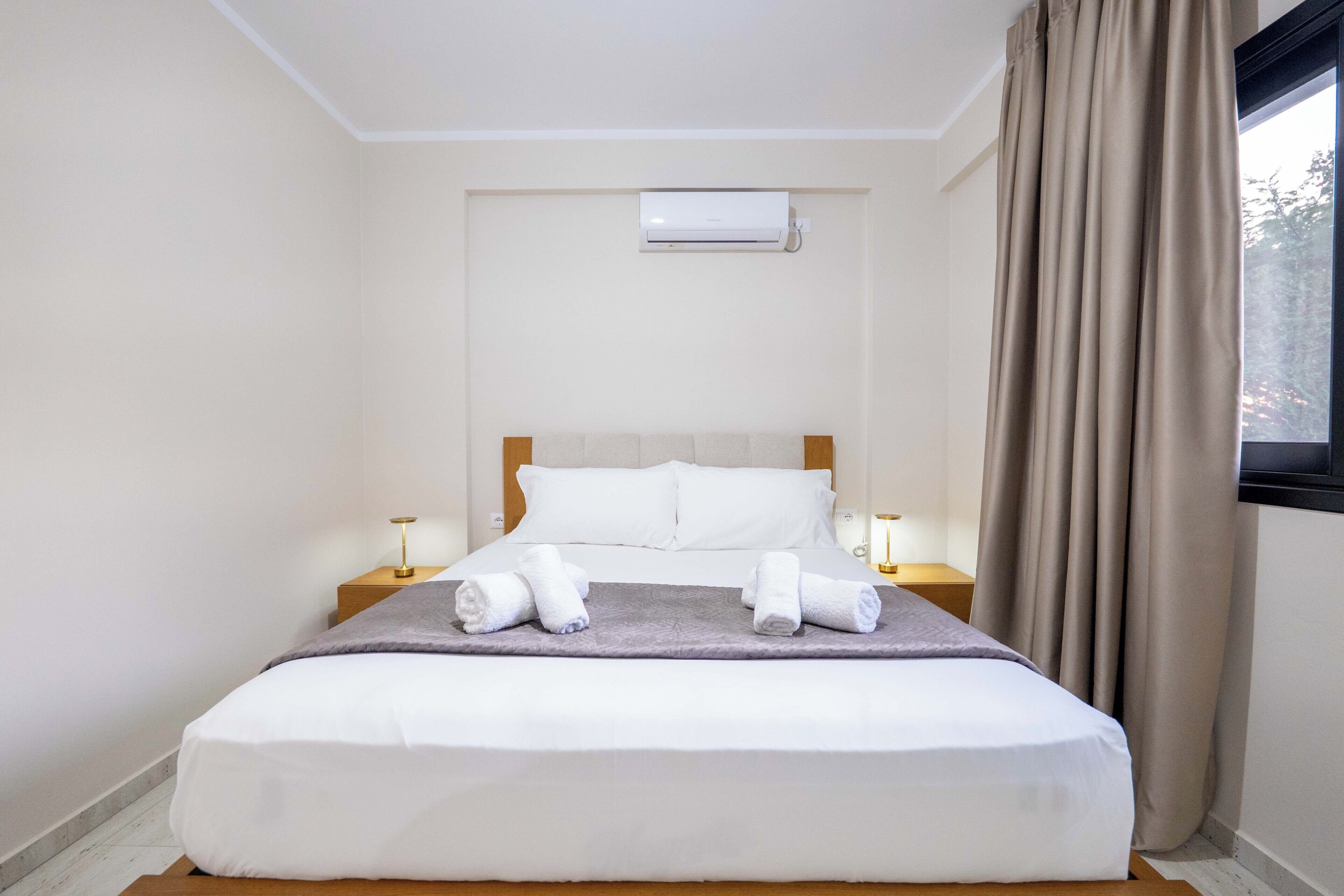 Een hotelkamer met een bed, twee nachtkastjes, een raam met gordijnen en een airconditioning.