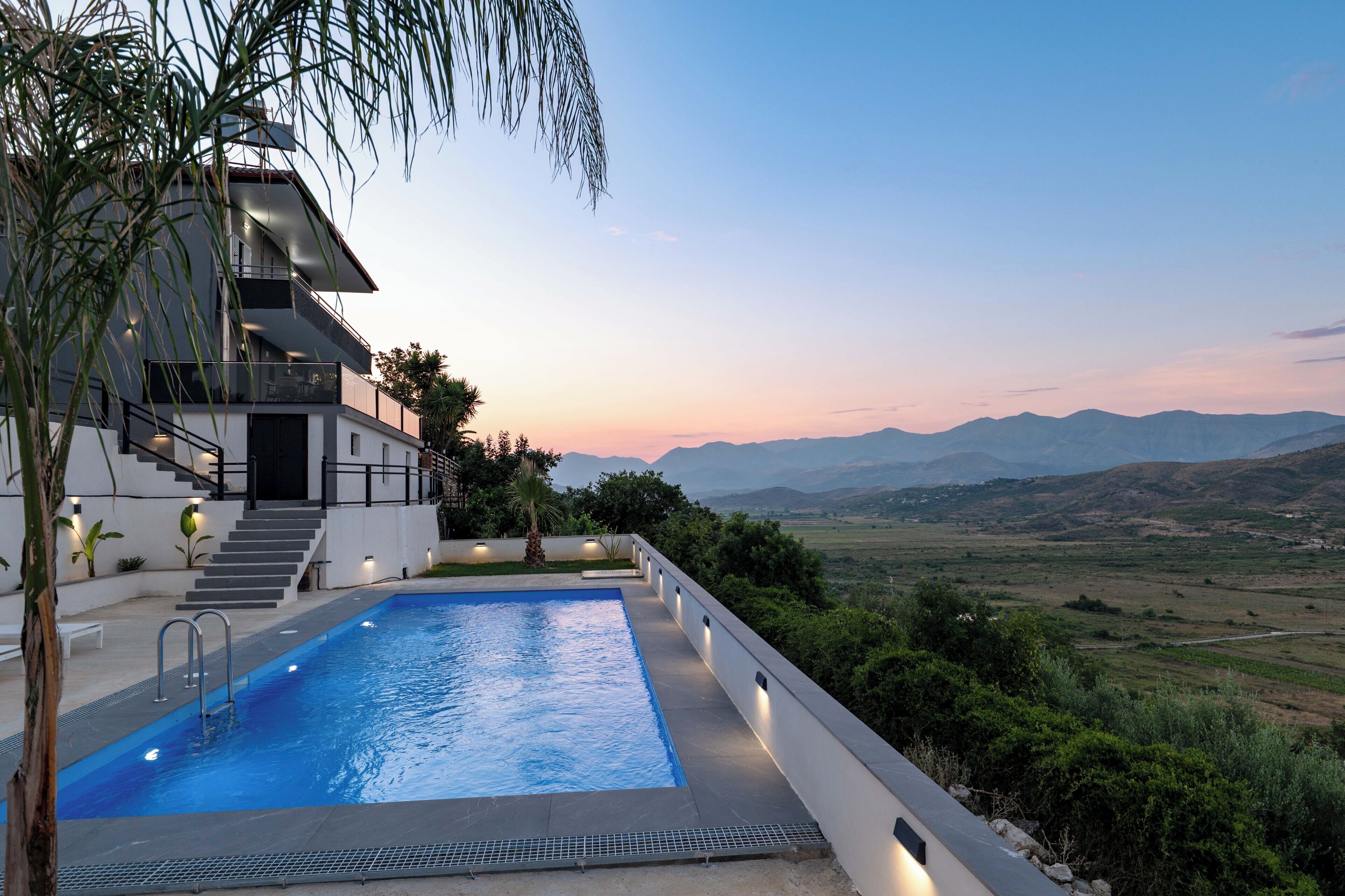 A modern building with a swimming pool, stairs, and a view of the mountains.