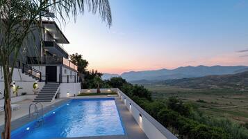 A modern building with a swimming pool, stairs, and a view of the mountains.