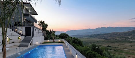 A modern building with a swimming pool, stairs, and a view of the mountains.