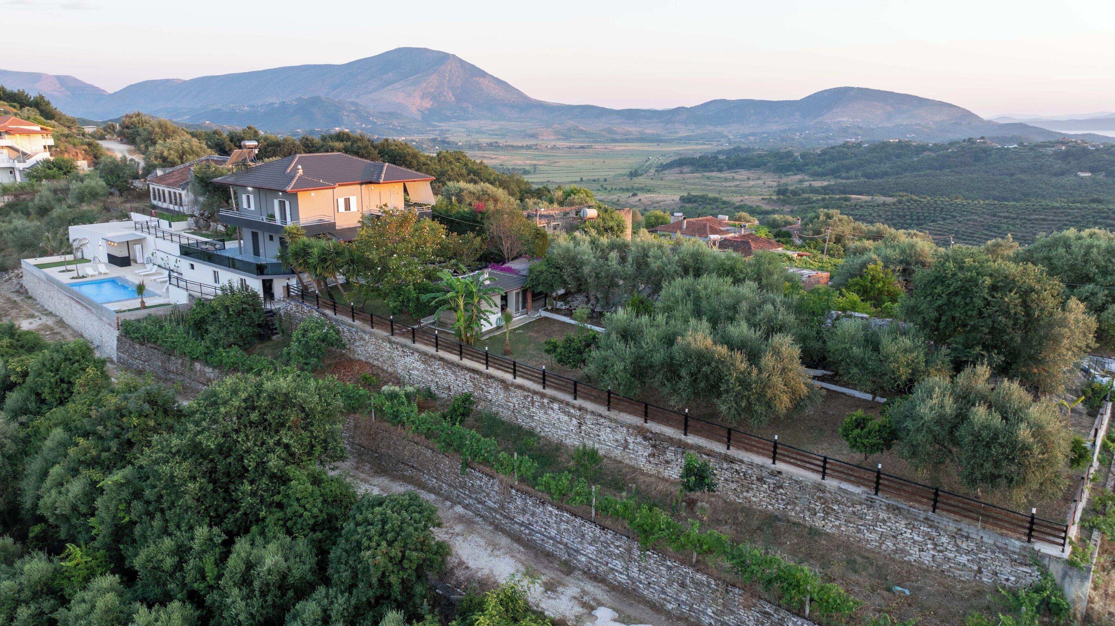 A modern house with a swimming pool, surrounded by lush greenery and mountains in the background.