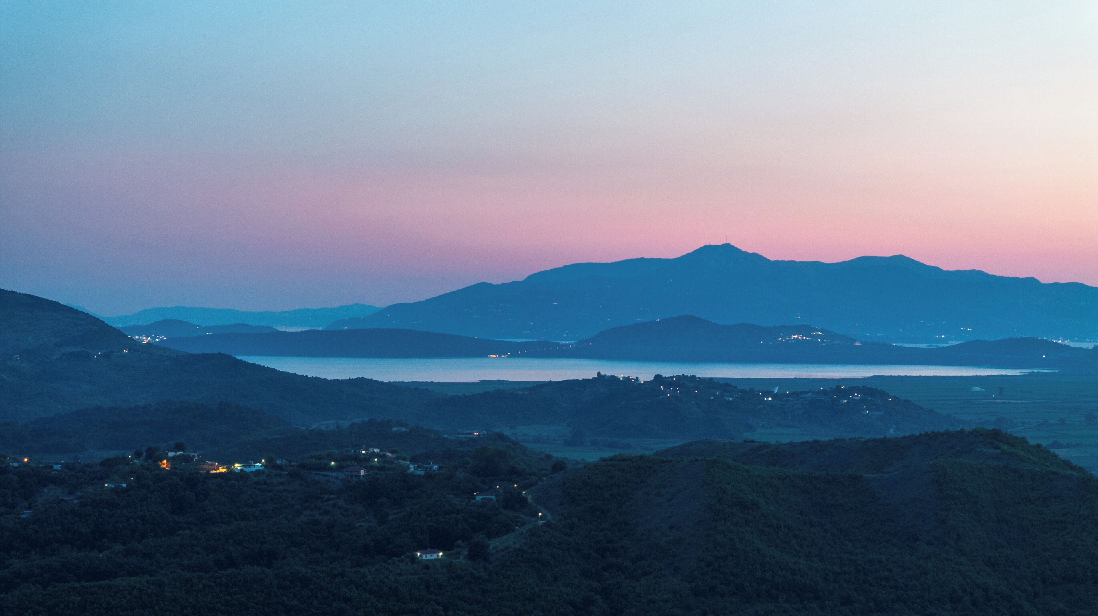 A mountainous landscape with a body of water and distant lights.