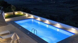 A rectangular swimming pool with a metal ladder, surrounded by a deck with steps and a few lounge chairs. - Villa Verde (Aliko)