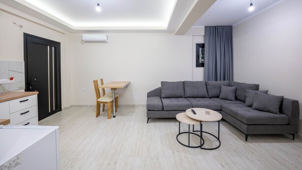 A modern living room with a grey sectional sofa, a small round table, and a dining area with a wooden table and chairs. - Villa Verde (Aliko)