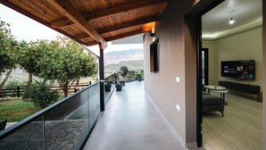 A balcony with a view of mountains, a stone floor, and a modern interior with a flat-screen TV. - Villa Verde (Aliko)