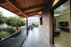 A balcony with a view of mountains, a stone floor, and a modern interior with a flat-screen TV.