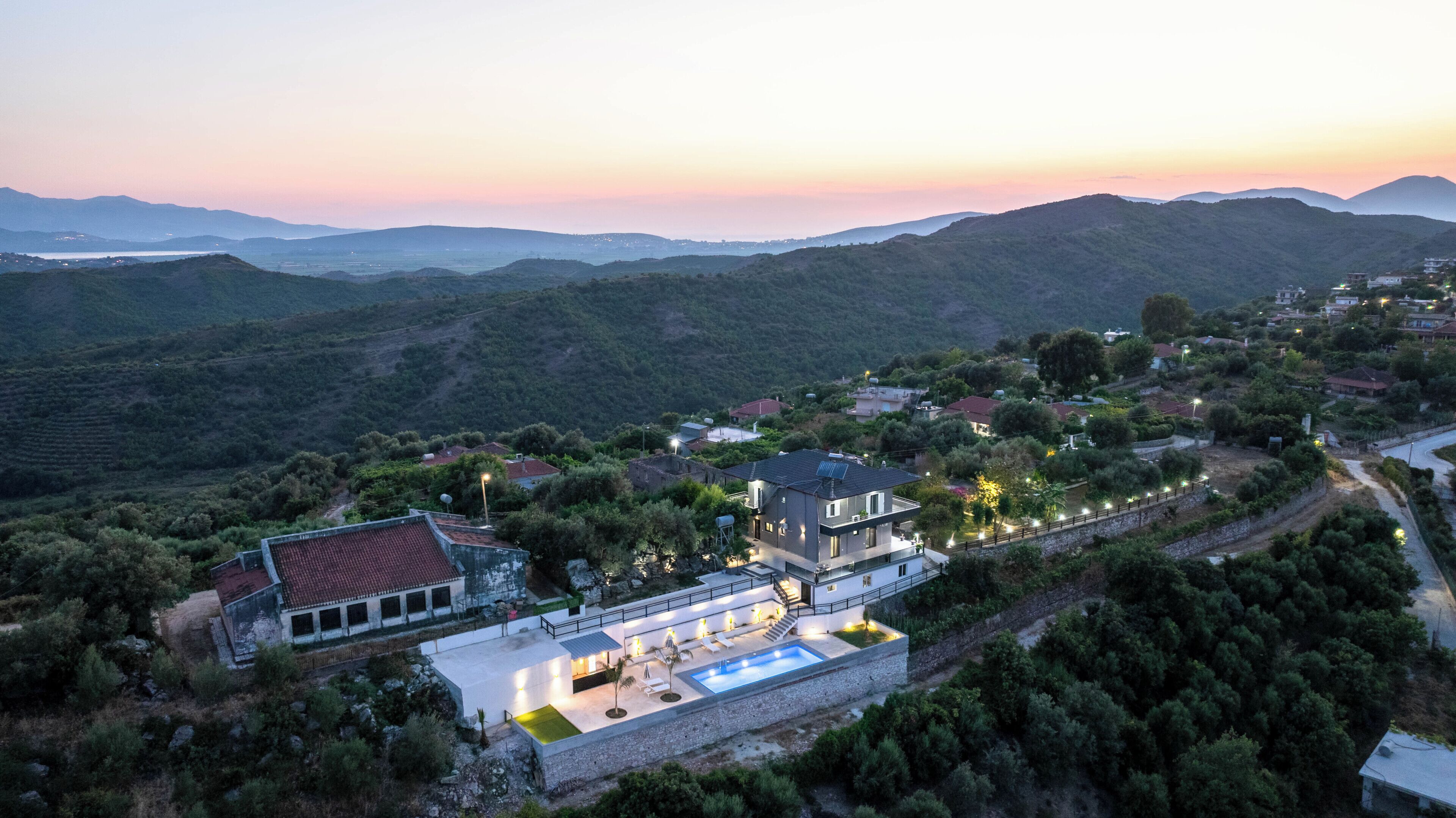 Eine moderne Villa mit Swimmingpool, umgeben von üppiger Vegetation und Hügeln.