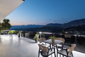 Una terraza con mesa y sillas, plantas en macetas y vistas a montañas distantes.