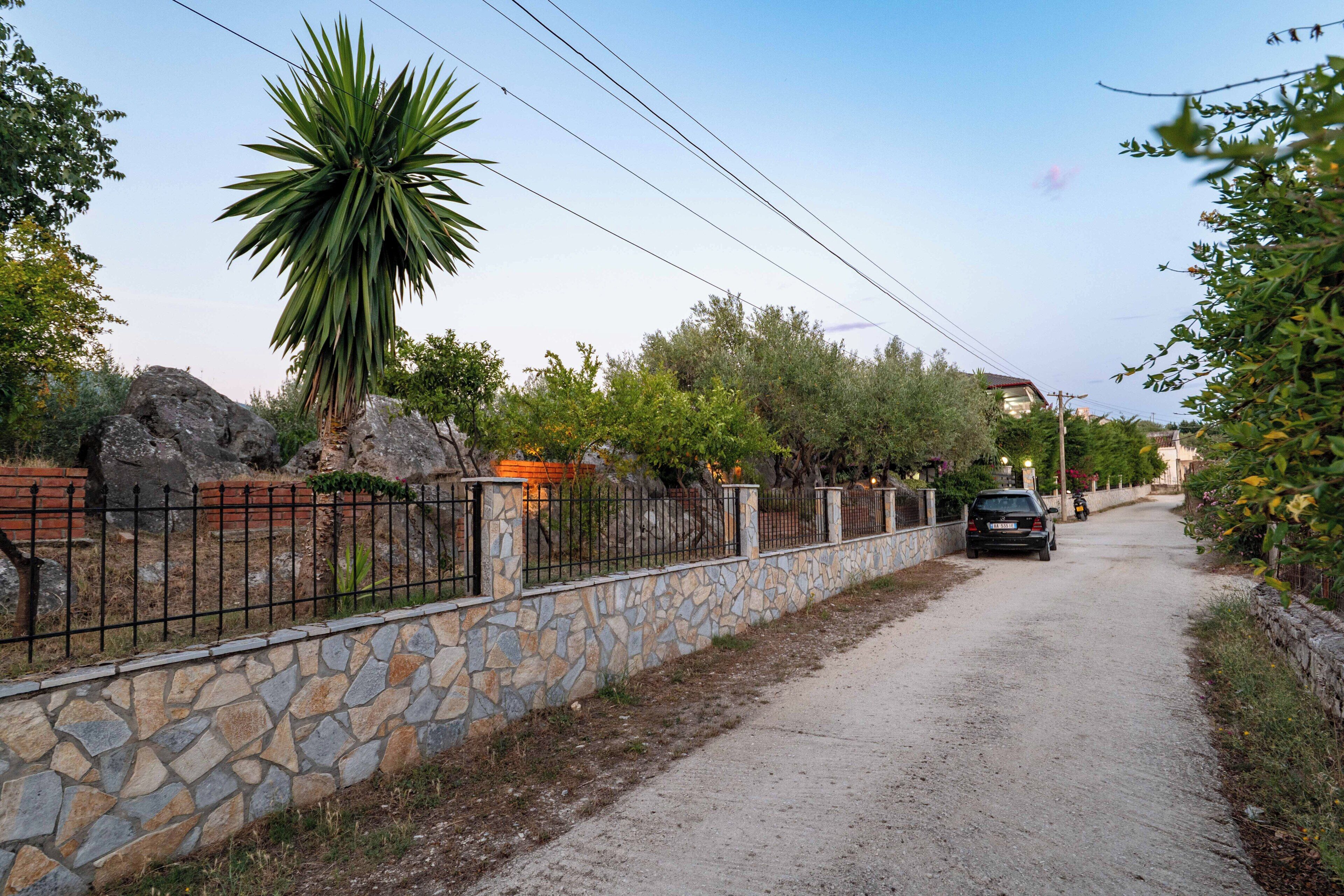 A paved path with a stone wall on one side and a metal fence on the other, leading to a parked car.