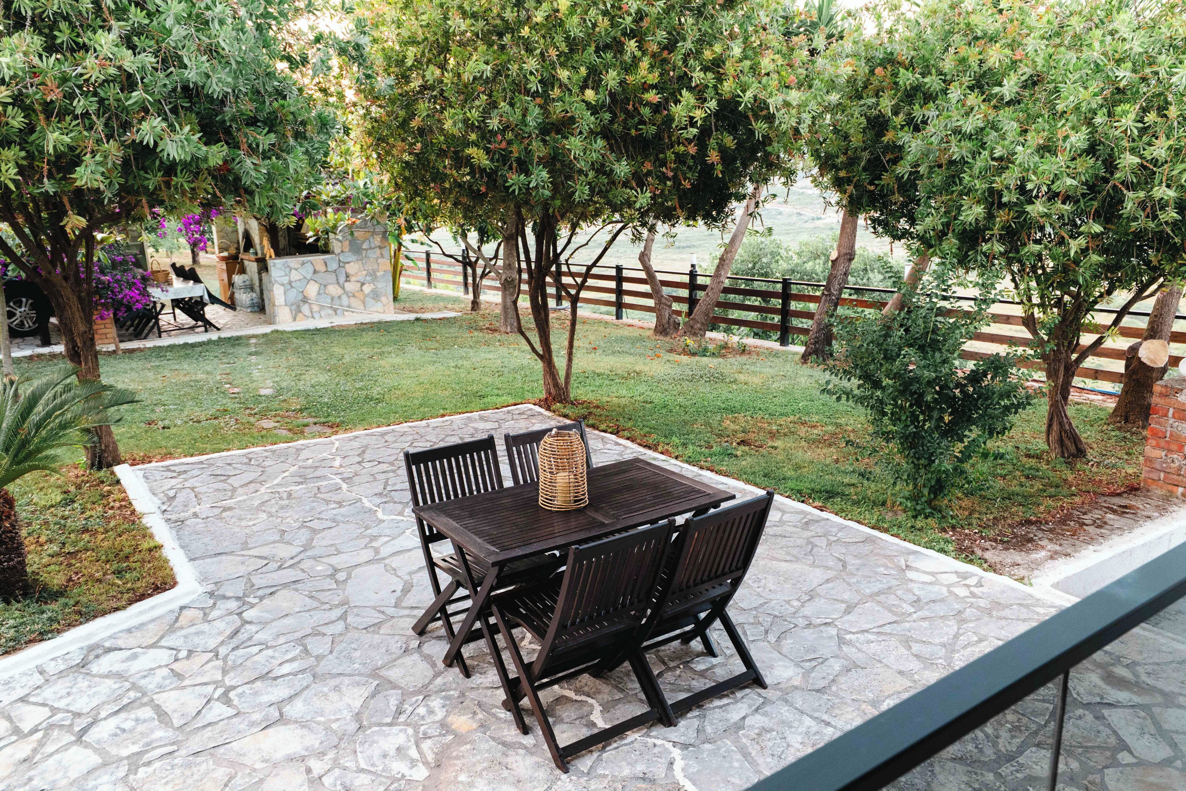 Eine Terrasse mit Steintisch und -stühlen, umgeben von Grünpflanzen und einer Steinmauer.