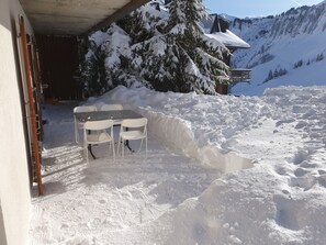 A snow-covered outdoor area with a table and chairs, a wooden structure, and a mountain backdrop. - Résid. Les Rhodos 1, (Les Crosets), by Interhome (Les Crosets)