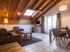 A cozy living room with a sloped ceiling, wooden beams, a flat-screen TV, a dining area with chairs, a coffee table, and a potted plant. - Patricia self-check-in Apartments, (Zermatt), by Interhome (Zermatt)