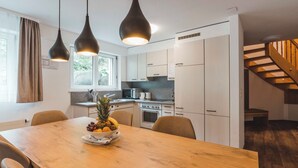 Una cocina moderna con armarios blancos, una mesa de comedor de madera con fruta e iluminación colgante.