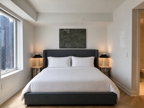 A modern bedroom with a large bed, two bedside lamps, a city view, and a framed artwork on the wall. - Nester Finn Downtown Toronto (Toronto)