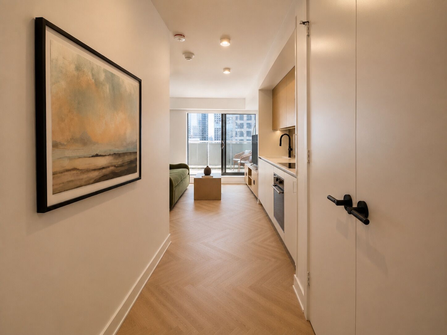 Un couloir orné d’un tableau, avec un canapé, une table basse et une vue sur un balcon donnant sur le paysage urbain.