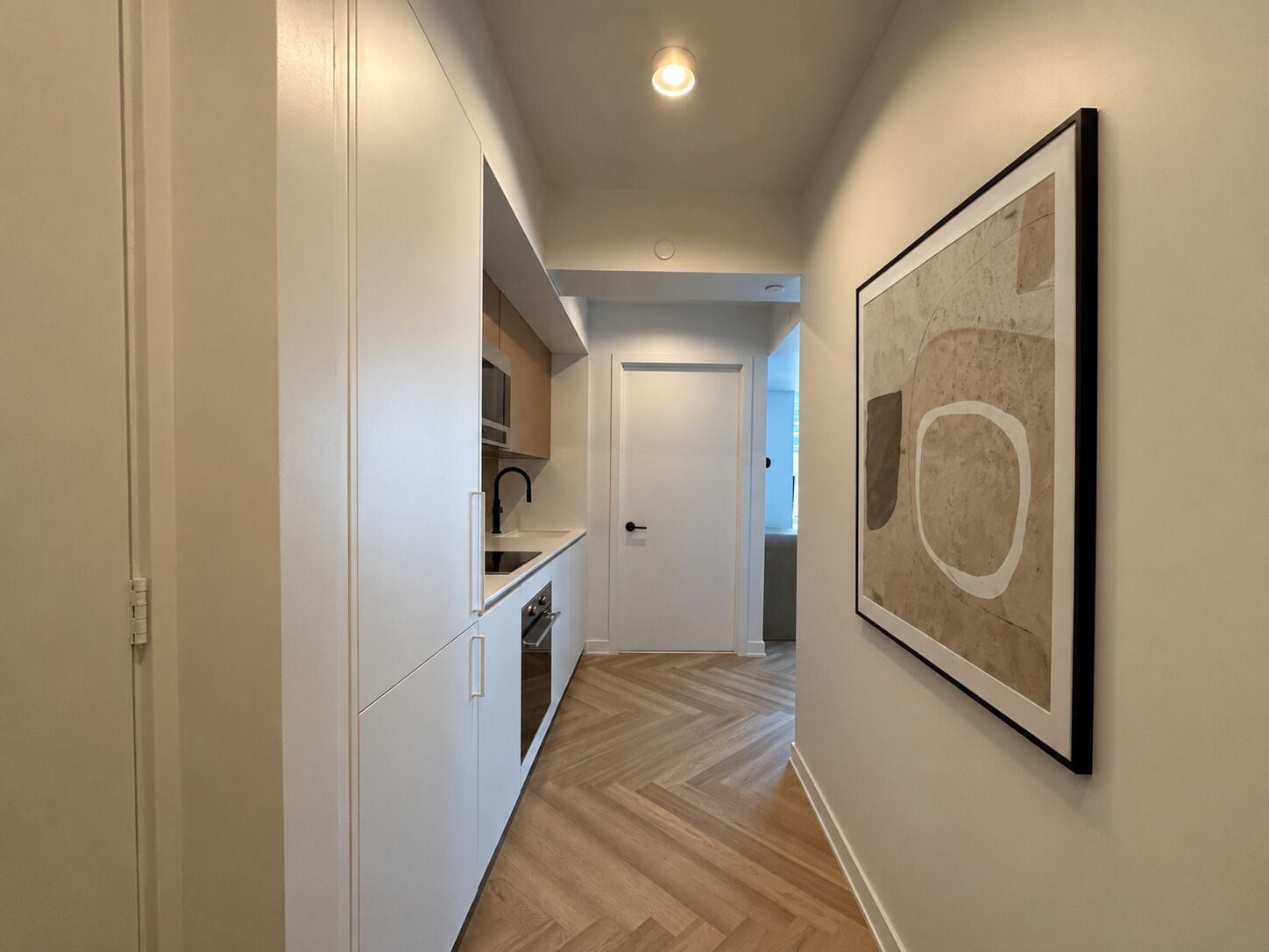 Un couloir comprenant un coin cuisine, une porte et une œuvre d’art encadrée accrochée au mur.
