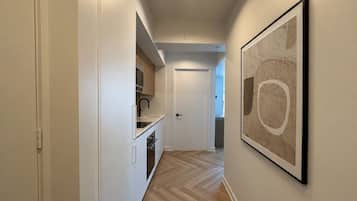 Un pasillo con una zona de cocina, una puerta y una obra enmarcada en la pared.
