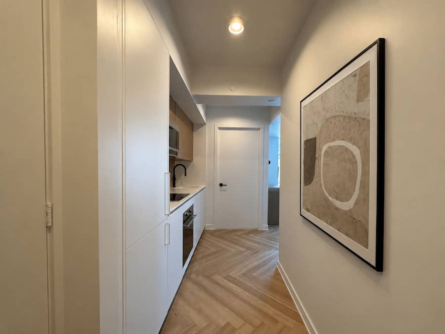 Un pasillo con una zona de cocina, una puerta y una obra enmarcada en la pared.