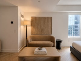 Een moderne hotelkamer met een bank, een nachtkastje met boeken, een lamp en uitzicht op de stad.