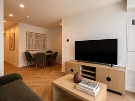 Een moderne woonkamer met een flatscreen televisie, een eethoek met stoelen, en een salontafel met boeken en een vaas.
