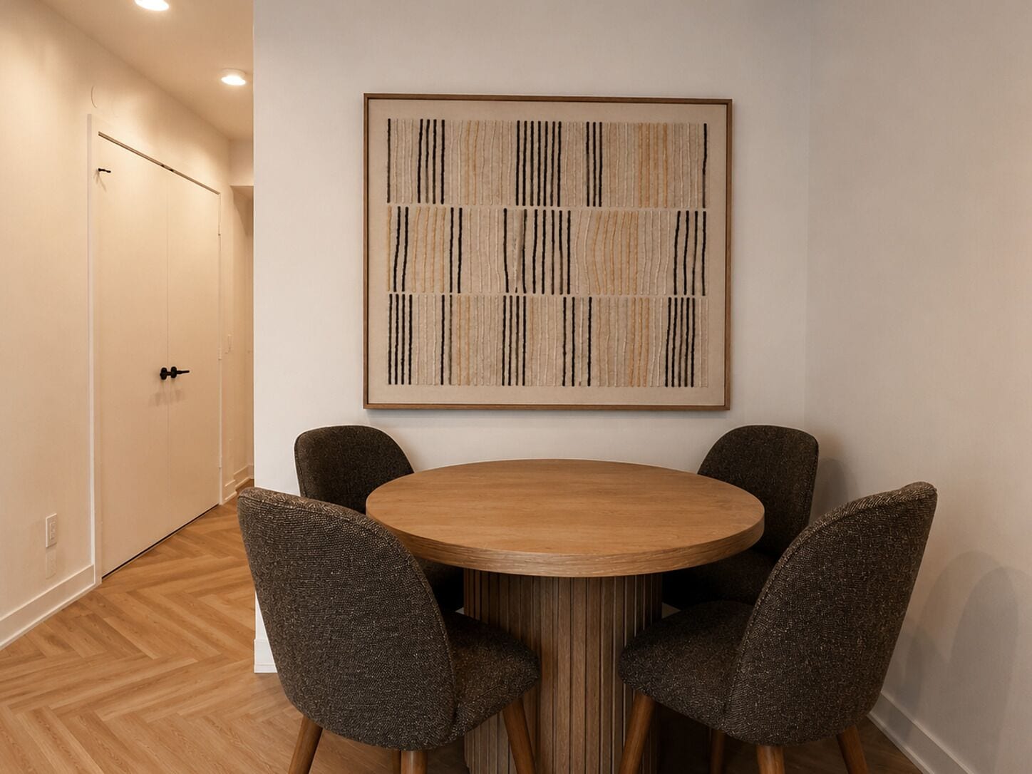 Un comedor con una mesa redonda de madera y cuatro sillas, una obra de arte abstracta enmarcada en la pared, y suelo de madera.