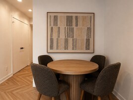Un comedor con una mesa redonda de madera y cuatro sillas, una obra de arte abstracta enmarcada en la pared, y suelo de madera.