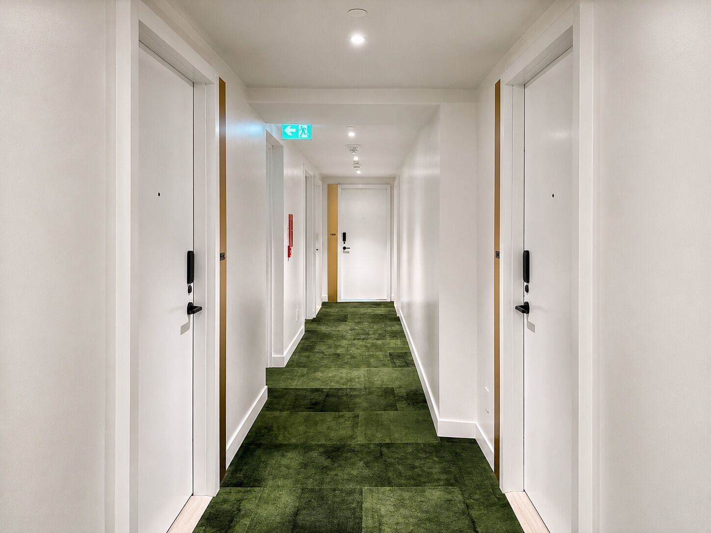 Un pasillo de hotel con paredes blancas, alfombra verde y puertas a ambos lados.