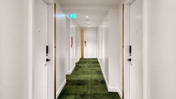 Un pasillo de hotel con paredes blancas, alfombra verde y puertas a ambos lados.