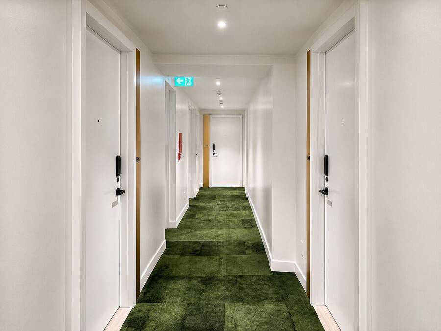 Un pasillo de hotel con paredes blancas, alfombra verde y puertas a ambos lados.