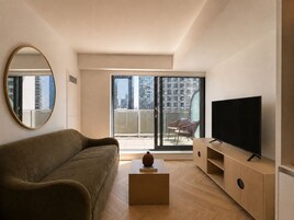 A modern living room with a sofa, a television, and a balcony with a view of the city.
